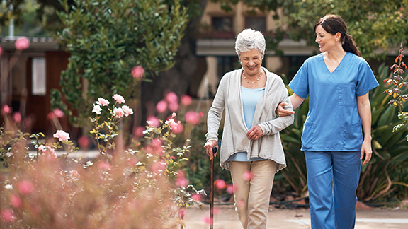 A nurse walking outside in a garden with her senior patient.