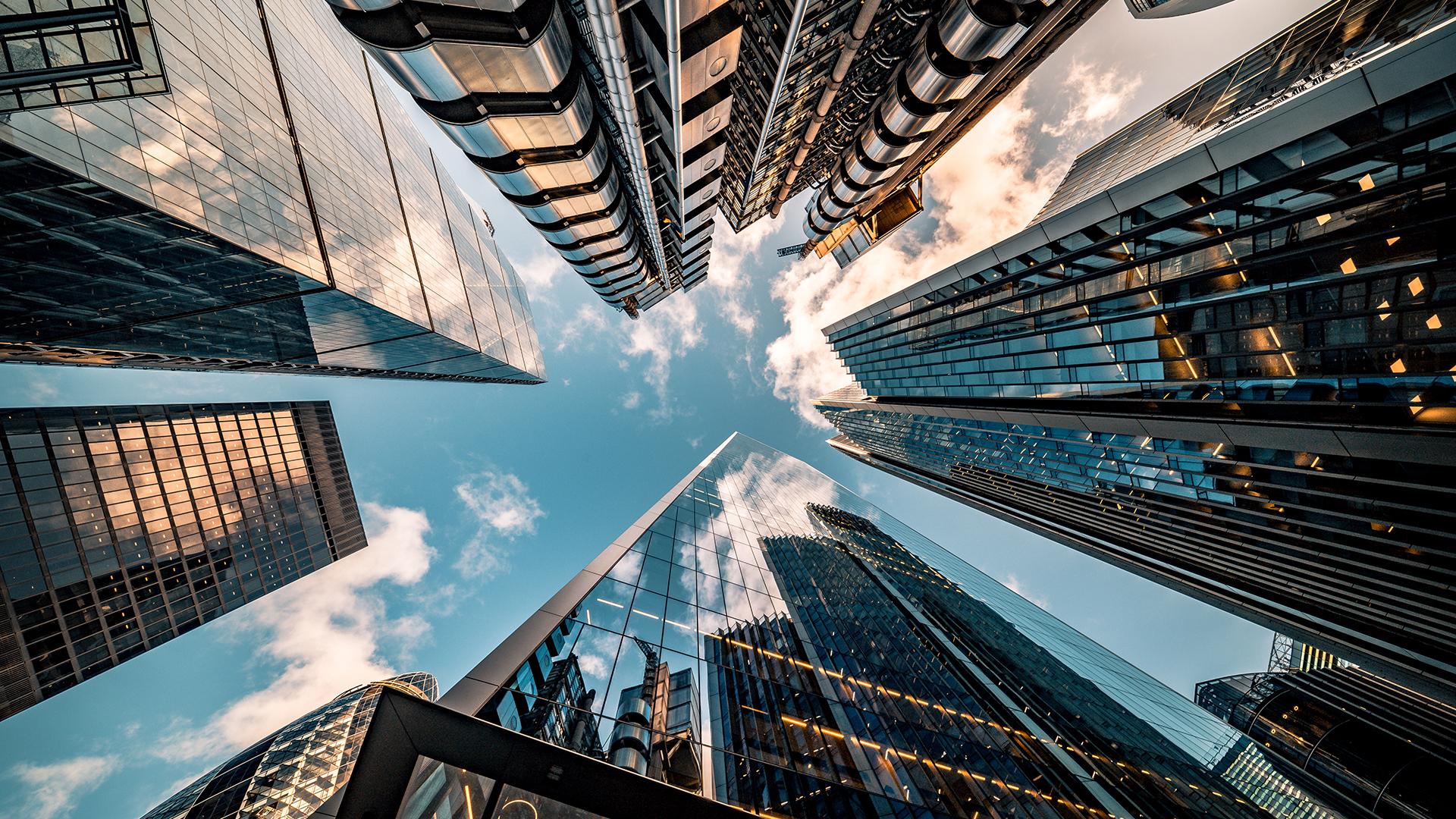 Looking up at a cluster of skyscrapers converging into a blue sky with clouds.